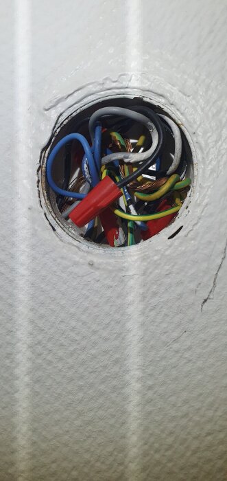 Elektrisk dosa med blandade kablar, inklusive blåa, gröna och kopparledare, inuti ett vitt vägguttag.
