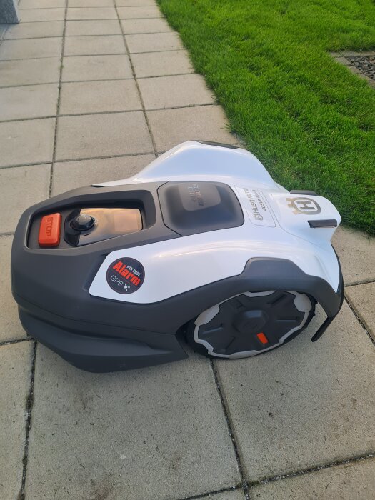 Robotgräsklippare Husqvarna Automower 405X placerad på en stenlagd gång bredvid en grönskande gräsmatta.