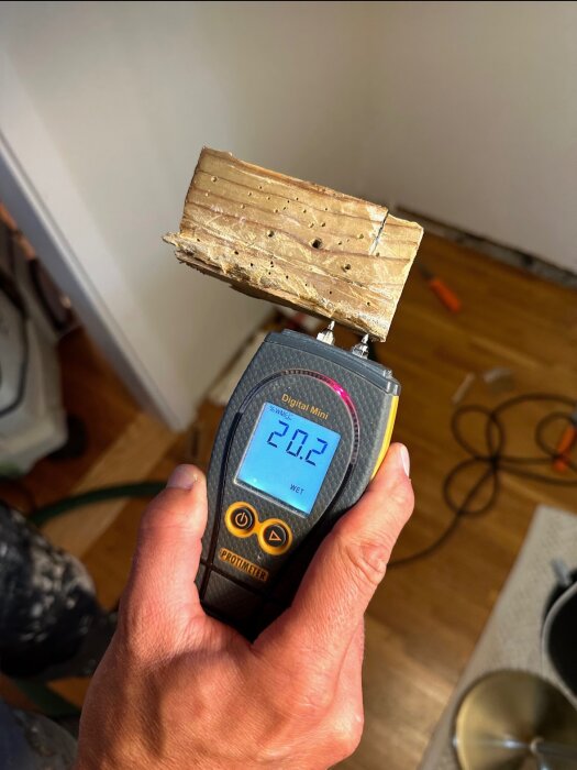 Fuktmätare visar 20,2% på ett trästycke i en byggmiljö.