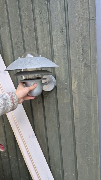 Utomhuslampa hålls mot grön trävägg, diskuteras för infälld installation med eluttag, obestämd lösning.