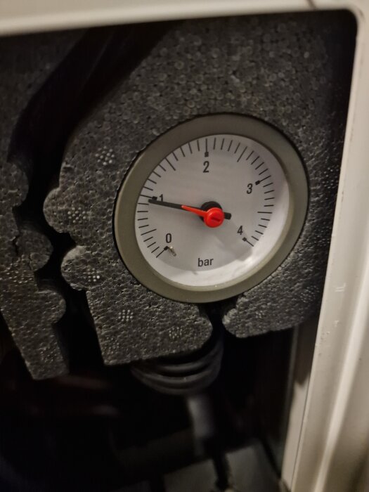 Manometer visar tryck i bar, nålen pekar på 1 bar. Omgiven av skyddande material.