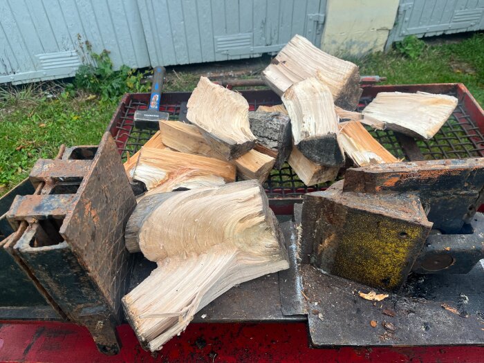 Vedklyv med klyvkil och tryckplatta, flera vedbitar ligger på klyvbordet utomhus, omgärdat av en röd metallram.