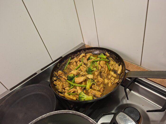 Kyckling och broccoli fräses i en stekpanna på en spis.