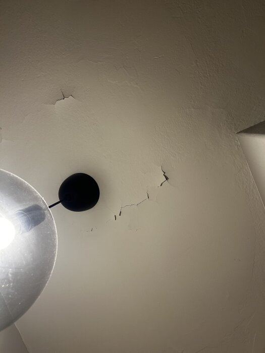 Tak med sprickor och avflagad färg i en lägenhet, belyst av en lampa.