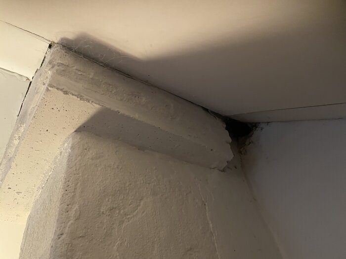 Hörn av ett rum med sprickor och skugga, vitmålad yta, oanvänd del i byggnadsrenovering.