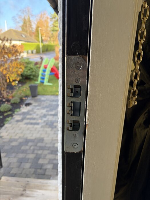 Närbild av en dörrkarm med ett nytt dörrlås installerat av en låssmed. Trädgård och gångväg syns i bakgrunden.
