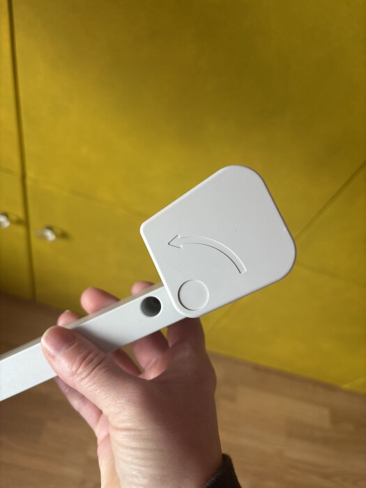 Hand håller i en vit del av en dammsugare med en skruv och ett vridbart lock. Bakgrund i gult.