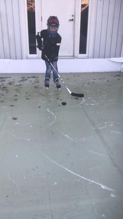 Ett barn utrustat med ishockeyutrustning spelar hockey på en hemmagjord isrink. En rolig och inspirerande aktivitet för vintersportentusiaster.