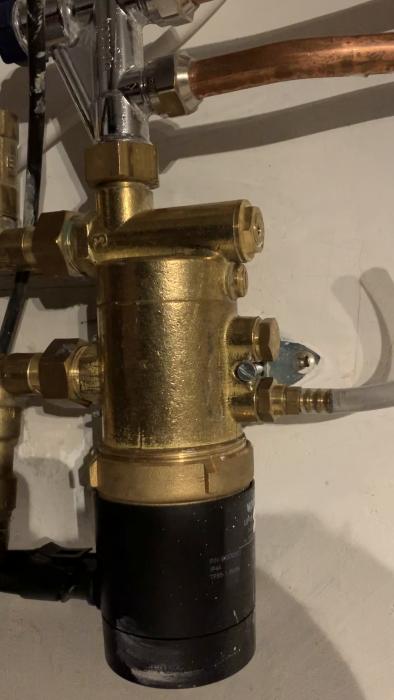 En film som visar en golvvärmepump i en källare som efter 4 års drift börjat avge ljud och 'varvar' upp några gånger varje timme. Systemet är kopplat till fjärrvärme och matar 5 slingor.