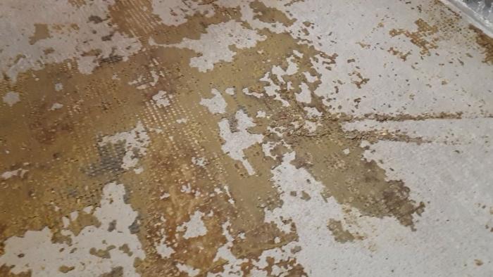 Se hur man tar bort golvlim efter en matta. Videon visar gult, sprött lim som skrapas bort från betonggolvet, samt gummi som fastnat från mattans baksida.