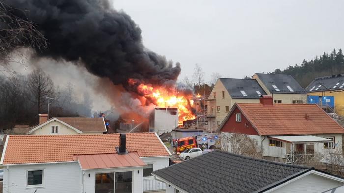 En allvarlig brand i en byggnad med tjock svart rök, brandmän på plats, i ett bostadsområde.