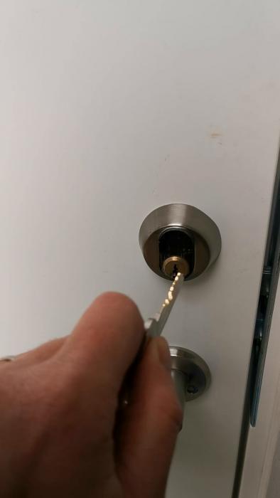 En person håller i en nyckel som är instucken i ett lås på en vit dörr.