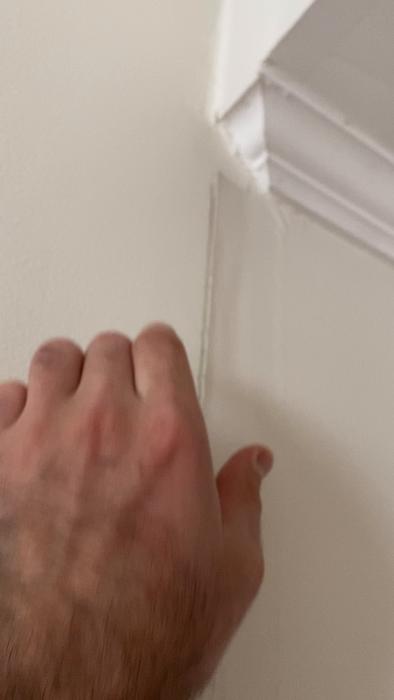 En hand drar bort ett vita tejptrikångel från en hörnlist vid en vägg.