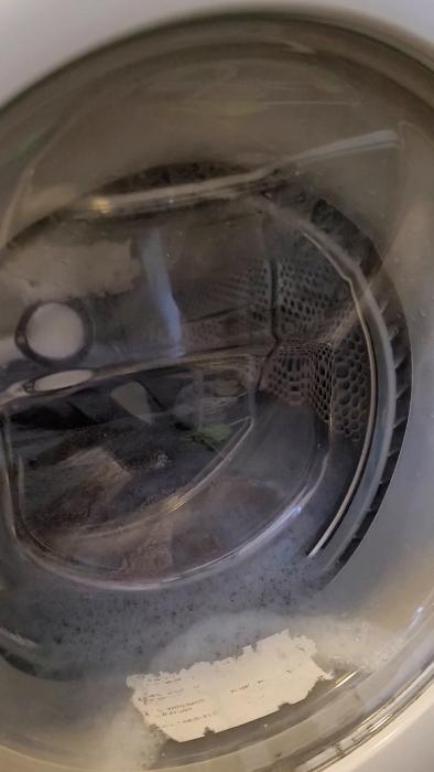 Tvättmaskin i drift med kläder och skum inuti, ett tuggat papper fastnar på dörrens insida.