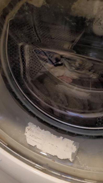En tvättmaskin trommel fylld med kläder, synlig genom luckans glass, med tvättcykel pågående och löst pappersbit framför.