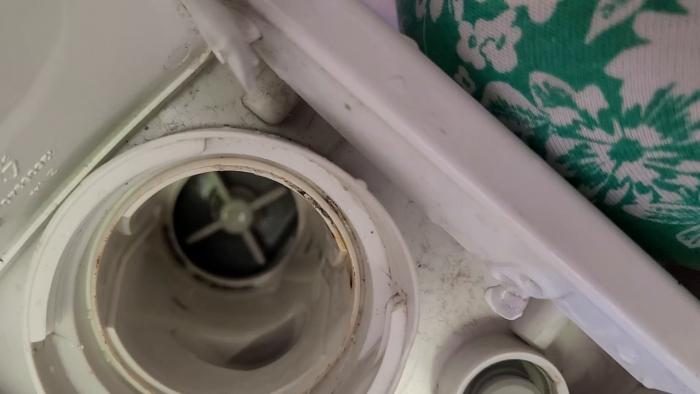 En skruvmejsel justerar eller reparerar någonting i en tvättmaskin, synlig smuts och en färggrann trasa.