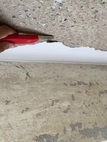 Ett finger applicerar vit fogmassa i ett hörn mellan en vit vägg och vad som ser ut som en stengolvyta.