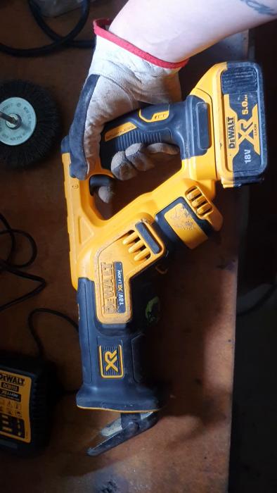 En hand i skyddshandske håller en gul och svart DEWALT XR batteridriven cirkelsåg på ett arbetsbord.