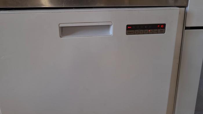 En person tömmer en diskmaskin med disk och bestick synliga i korgarna.