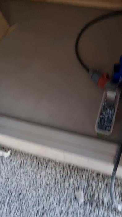 Videobild av en oinredd inomhusmiljö med isoleringsmaterial på väggarna, trästomme och kablar på ett betonggolv.