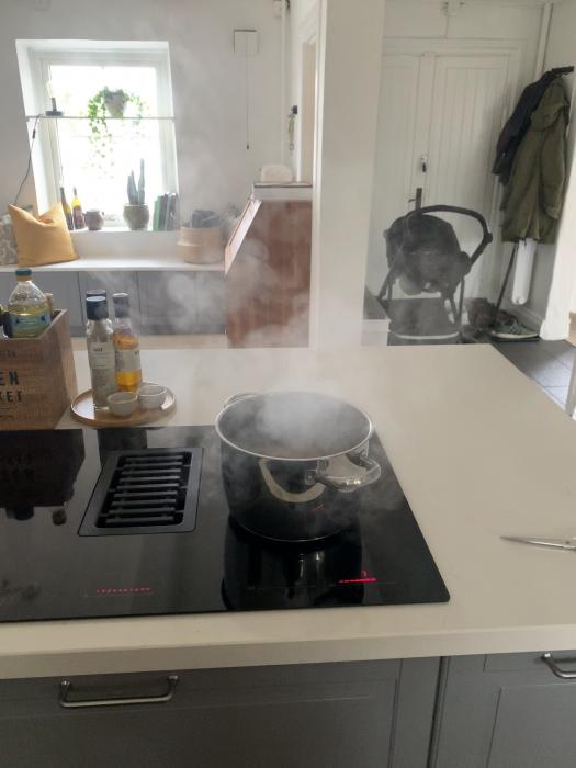 En kokande kastrull på en induktionshäll i ett modernt kök, med ånga som stiger upp.
