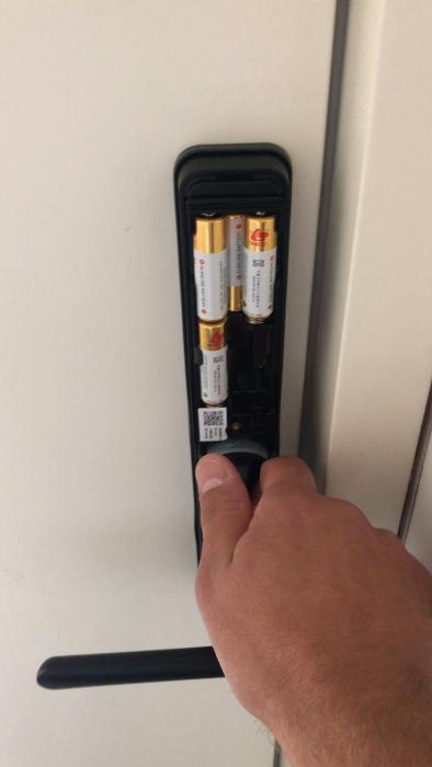 Ett dörrhandtag med AA-batterier i batterifacket, en hand rör vid handtaget.