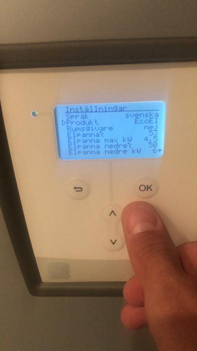 Ett finger trycker på en knapp under en LCD-display med installationsinställningar på svenska för en uppenbar uppvärmningsenhet.
