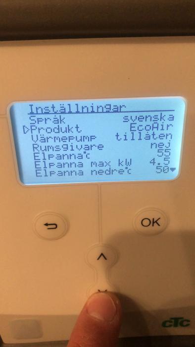 En hand trycker på en pil upp-knapp under en LCD-skärm, visa inställningsmenyn på svenska för en elektronisk enhet.