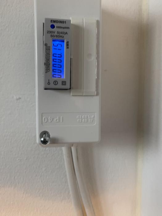 Digital elmätare fastmonterad på vägg med LCD-display och kablar anslutna nedtill. Visar elförbrukning i kilowattimmar (kWh).