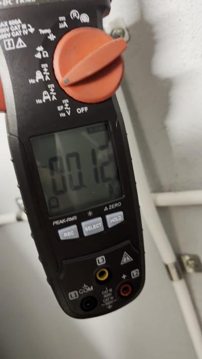 Multimeter visar 0.975 på displayen. Verktyget används för elektriska mätningar. Röd och svart tangentiell design framträder.