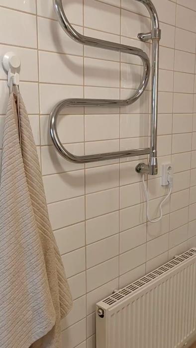 En vit stängd dörr med ett dörrhandtag i mässing, bredvid en vit kaklad vägg med en handduk.