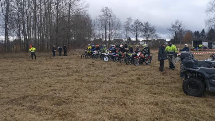 Motorcyklister förbereder sig för start i ett terränglopp, med en funktionär som håller i en röd flagga.