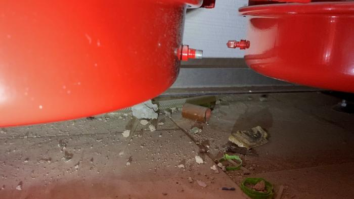 Röda maskindelar i närbild med metalldetaljer, slangar och små spillbitar på en grå yta.