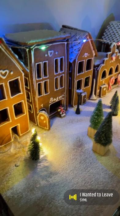 En miniatyrjulby med pepparkakshus, små granar, och svagt upplyst snötäckt gata. Christmas-themed miniature village with gingerbread-style houses, tiny fir trees, and softly illuminated snow-covered path.