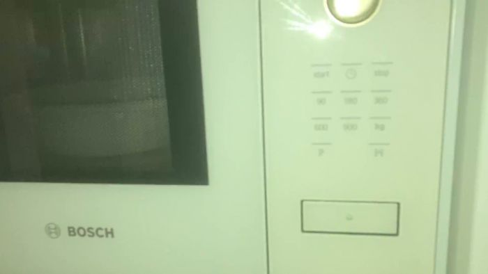 En person trycker på en knapp på en vit Bosch-mikrovågsugn eller ugn med olika inställningar synliga.
