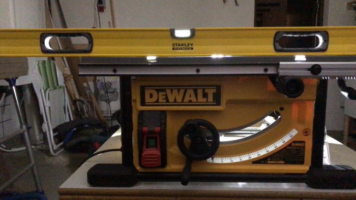 En person använder en gul och svart DEWALT kap- och geringssåg med ett STANLEY vattenpass ovanpå för att kontrollera horisontell nivå.
