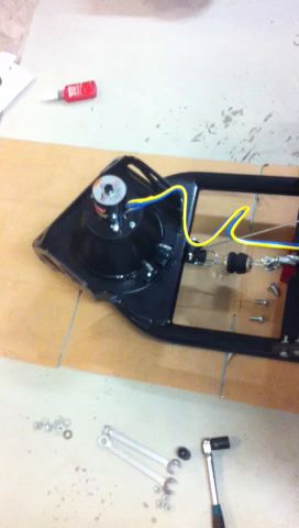 Ett elektroniskt projekt på ett bord, inklusive en svart plastdel med kablar, ett öga-liknande objekt, och verktyg som skruvmejsel samt lösa komponenter.