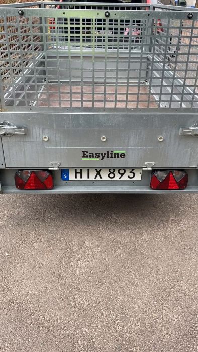 Ett släp med en gallerbur registreringsskylt "HTX 893" under texten "Easyline", synlig på en asfalterad yta.