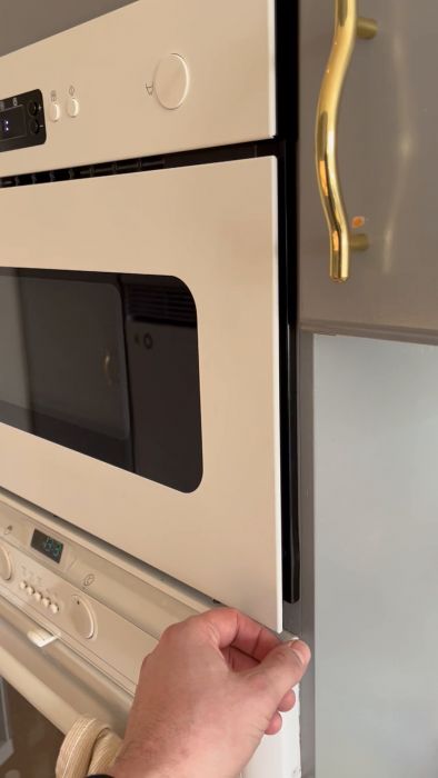 Ett modernt kök med öppet bänkdiskmaskinens lucka avslöjar glänsande rena tallrikar inuti; guldfärgat handtag syns på luckan.