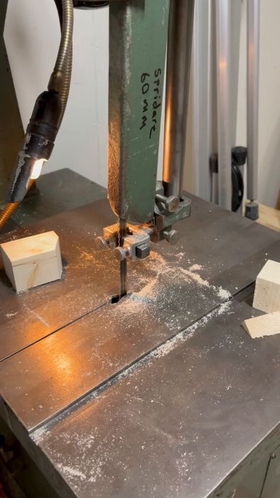 En bandsåg genom ett skärningsögonblick, sågspån spridda, träblock på sidan, fokus på sågens blad och arbetsstycket.