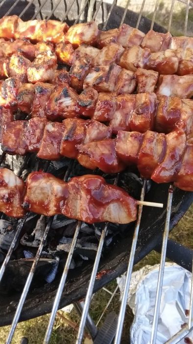 En grill med marinerade kycklingspett och en folieform med lök och svamp vid sidan.