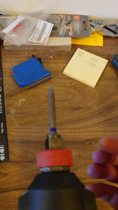 En suddig film som visar en hand hålla i en skruvmejsel, placerad på toppen av en röd och svart borrmaskin eller skruvdragare.