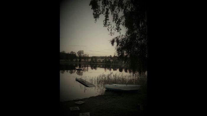 En stämningsfull film med texten "Glad midsommar!", en sjö, en flytande brygga och en roddbåt vid strandkanten.