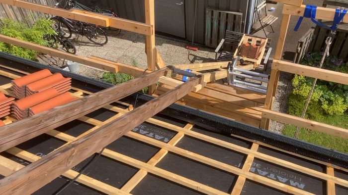 Film på en byggnadsplats med träreglar, takpannor och olika byggnadsverktyg i soligt väder.