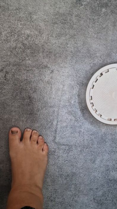 En bar fot bredvid en vit robotdammsugare på grå matta.