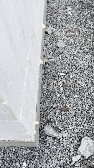 En närbild på hörnet av en byggnad under konstruktion med synligt isoleringsmaterial och byggavfall i bakgrunden.