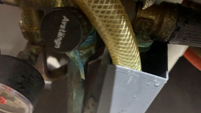 Närbild på vattenledningar och kopplingar med texten 'Afsäkron' synlig på en svart plastkork.