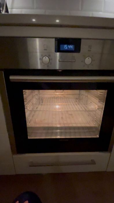 Ugnens kontrollpanel med suddig handrörelse, vredet i förgrunden, upplyst display som visar tiden "15".