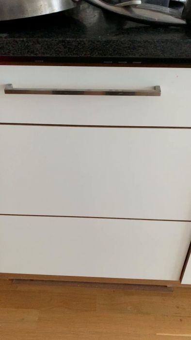 Kökslådor med metallhandtag, bänkskiva ovanför, trägolv nedanför, suddiga köksredskap syns ovan.