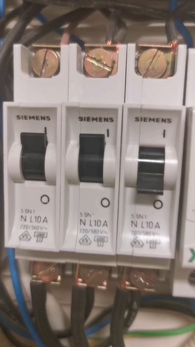 En hand rör vid en Siemens säkringsbrytare i ett elektriskt säkringsskåp, redo att slå om den.